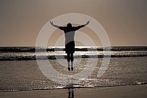 Silhouette of man jumping on beach. Amazing view on sunset beach.