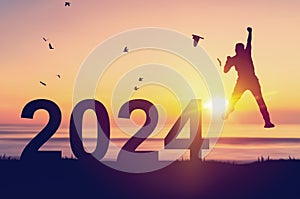 Silhouette man jumping and birds flying with number like 2024 at tropical beach on sunset sky abstract background. Happy new year