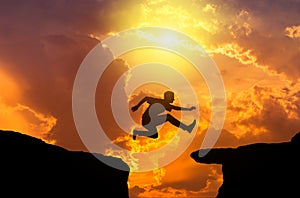 Silhouette the man jumping through the gap over rock cliff between mountain on sunset