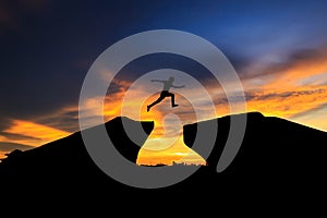 Silhouette of man jumping over cliff on sunset background