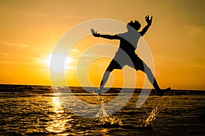 silhouette of a man in a jumping position In the sea at sunse