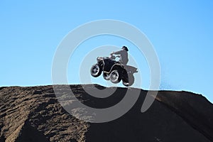 silhouette of a man jumping with a quad against a blue sky