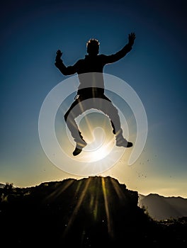 Silhouette of a man jumping on top of a mountain