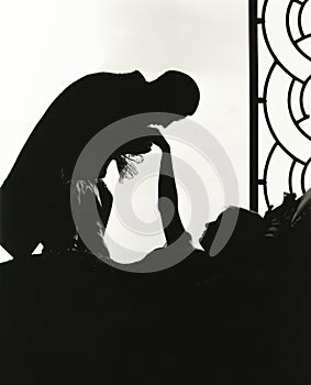 Silhouette of man kissing reclining woman's hand