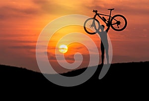Silhouette the man lifting mountain bike bicycle above his head on sunset