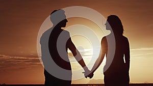 Silhouette man in love takes woman by hand and they look at each other with love. Couple in love on romantic date on