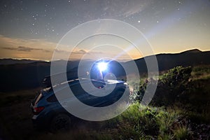 Silhouette of man at offroad car with head flashlight on background of very beautiful night starry sky after sunset