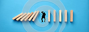 Silhouette of a man in panic try to protect himself against collapsing wooden dominos on blue background. Business crisis and