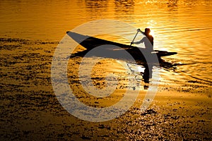Silhouette of a man peddling in a boat at sunset
