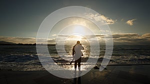 Silhouette of a man photographing the wave. Tourist photographer shoots stormy sea on wet embankment