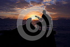 Silhouette man playing a guitar on the boat with blue sky sunrise