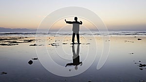 Silhouette of man practiceing qigong exercises at sunset by the sea.