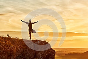 Silhouette of the man practicing yoga on the hill against beautiful sunset.