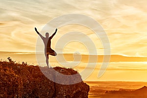 Silhouette of the man practicing yoga on the hill against beautiful sunset.