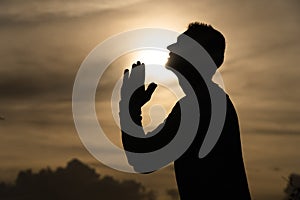 Silhouette of Man pray on during sunset. Repentance, regret and hope concept