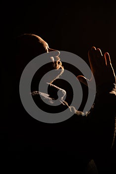 Silhouette of a man in prayer. The man folded his hands in communion with God. Dark background