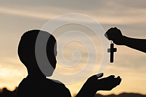 Silhouette of a man praying with a cross in hand at sunrise,  religion concept