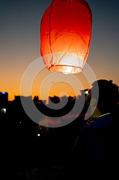 silhouette of man pushing up paper sky lantern with flame at bottom at sunset on sankranti uttarayan, independence day