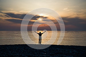 Silhouette of a man with raised arms in the sea water at sunset