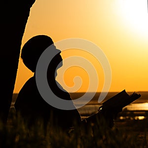 Silhouette of a man reading the Bible in the field, male praying to God in nature, the concept of religion and spirituality