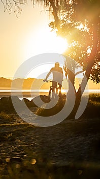 Silhouette of Man Ride a Bicycle at the Coast in Summer at Sunset Background in Noosa, Australia