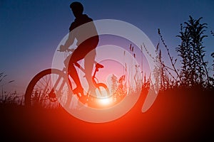 Silhouette of man riding bicycle in sunset sky background