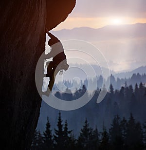 Silhouette of man rock climbing on straight vertical rock at sunrise. Side view. Extreme challenging ascent. Copy space