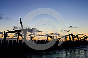 The silhouette of a man among the ruined old pier in the background light against the sunset