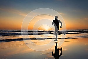 Silhouette of a man running on a beach at sunset.