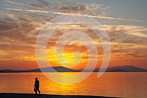 Silhouette of a man on the shore of the lake at sunset. Sunset over the sea with dramatic sky and reflection in the water