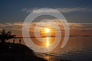 Silhouette of a man on the shore of the lake at sunset. Sunset over the sea with dramatic sky and reflection in the water