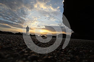 The silhouette man sits on a cliff above the sea and watching the sunset