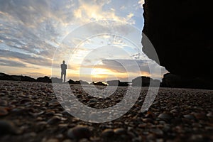 The silhouette man sits on a cliff above the sea and watching the sunset