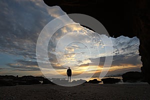 The silhouette man sits on a cliff above the sea and watching the sunset