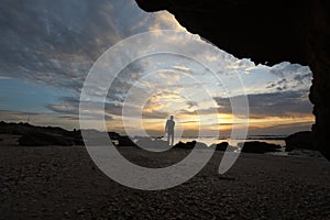 The silhouette man sits on a cliff above the sea and watching the sunset