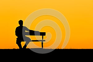 A silhouette of man sitting on bench in sunset