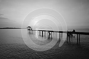 Silhouette of a man sitting on the bridge alone in black and white mode.