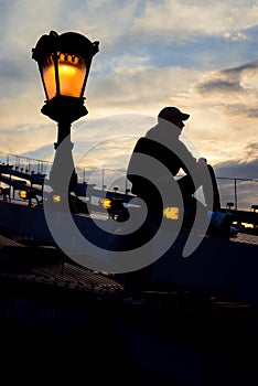 The silhouette of the man sitting on the Chain Bridge in Budapest, Hungary near the lightning street lamp.