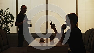 Silhouette of man sitting at the fast food bar holding reading social media on smartphone, waitress coming at the back.