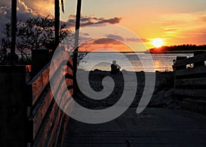 Silhouette of man sitting in sand watching a deep orange sunset over horizon at Sombrero Beach in Marathon Key