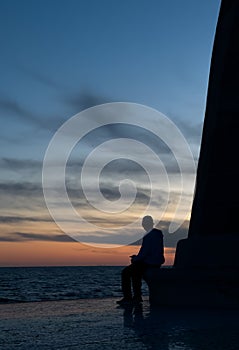 Silhouette of a man sitting on a structure watching the sunset