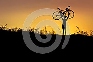 Silhouette the man stand in action lifting bicycle above his head with sunset