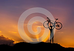 Silhouette the man stand in action lifting bicycle above his head with sunset