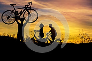 Silhouette the man stand lifting bicycle above his head with little boy and little girl riding bike on sunset