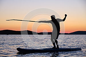 Silhouette of man on stand up paddleboard at sunset, pointing the paddle in a fencing position. Summer sport activities in Croatia