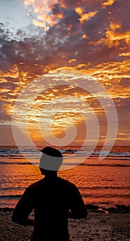 Silhouette of a man standing on the beach looking at the sunset which emits a golden triangular glow at dusk.