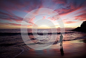 Silhouette of the man standing on the beach at sunset.