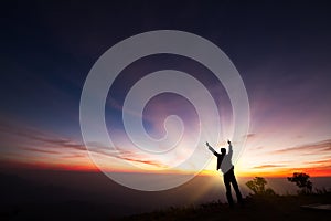 Silhouette of a man standing on the cliff looking at sunrise background, hope and following a dream concept