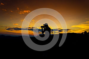 Silhouette Man Standing on Hill with  Camera at the Sunset on Mountain with Orange Sky. Enjoying Peaceful Moment Concept