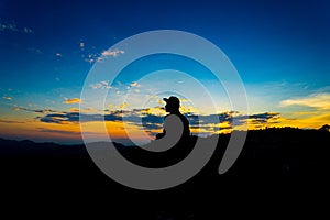 Silhouette Man Standing on Hill with  Cap at the Sunset on Mountain with Blue Sky. Enjoying Peaceful Moment Concept